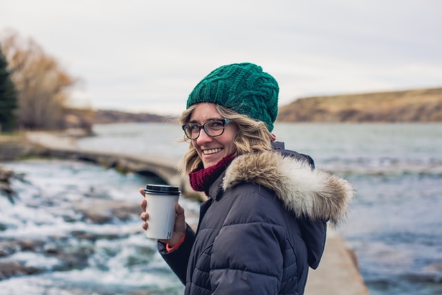 Woman standing outdoors in a moderately cold spring morning wearing a Volt heated jacket and drinking coffee, showing comfort and warmth